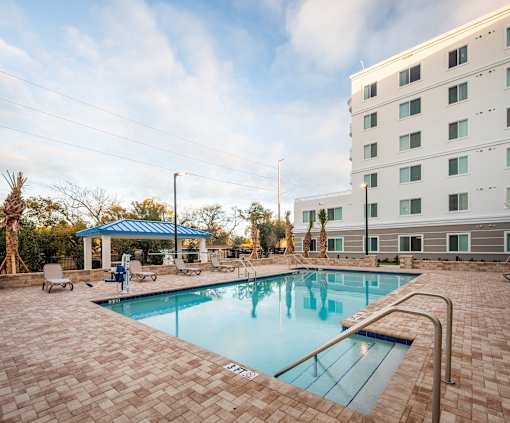 A swimming pool surrounded by a brick patio and a white building in the background.
