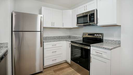 A kitchen with a stainless steel refrigerator, microwave, oven, and cabinets.