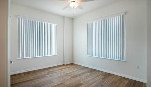 A room with wooden floors and two windows covered with blinds.
