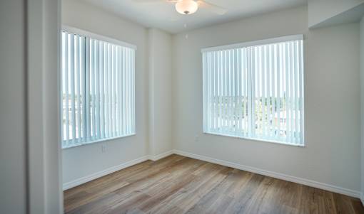 A room with wooden floors and two windows with blinds.
