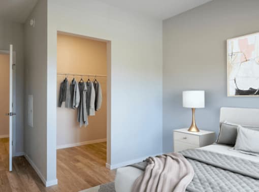 A bedroom with a bed, nightstand, and clothes hanging on a rack.