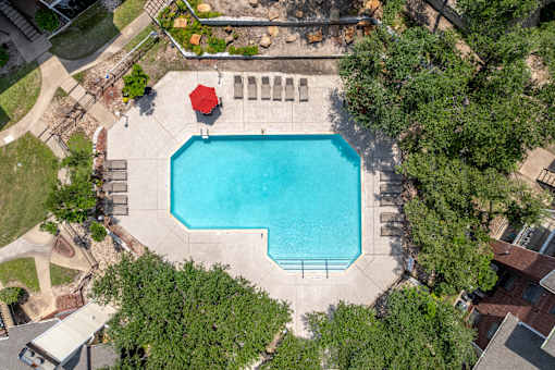A red umbrella sits on the edge of a blue swimming pool.
