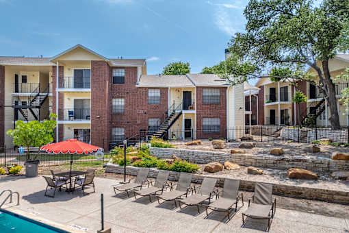 A pool area with chairs and a red umbrella in front of apartment buildings.