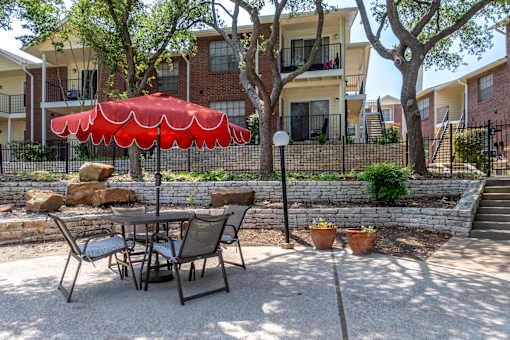 A patio with a table and chairs and a red umbrella.