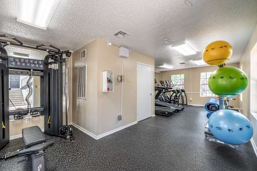 A gym with a variety of equipment including a treadmill, weights, and exercise balls.