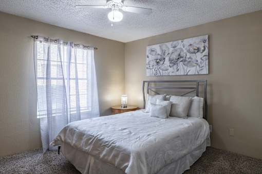 A bedroom with a bed, pillows, a ceiling fan, and a painting on the wall.