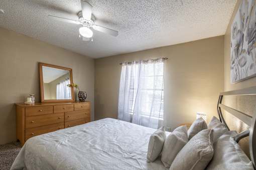 A bedroom with a bed, dresser, mirror, and a ceiling fan.
