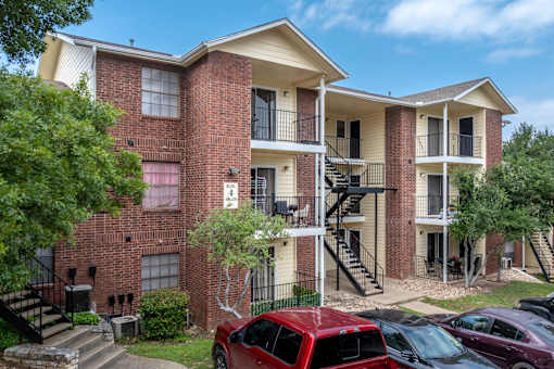 A red car is parked in front of a brick apartment building.