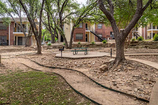 A park with a bench and a tree in front of apartment buildings.