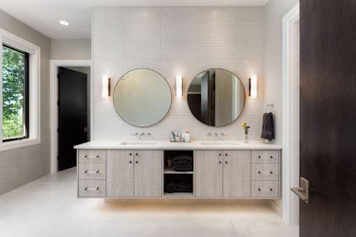 A bathroom with two round mirrors and a vanity with drawers.