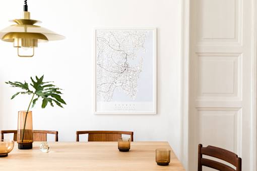 A dining room with a wooden table, chairs, a plant, a lamp, and a framed map on the wall.
