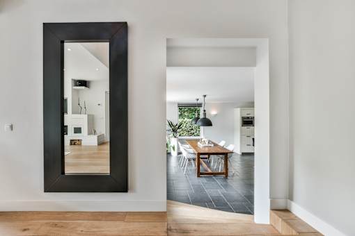 A large mirror on the wall reflects a living room with a dining table and chairs.