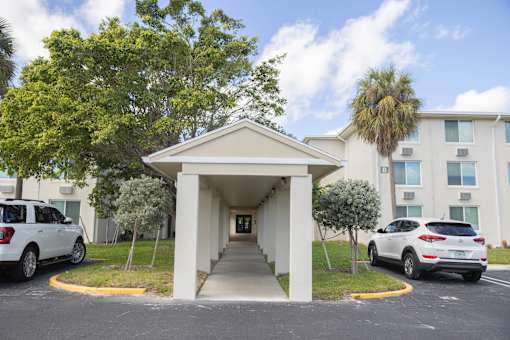 A white car is parked in front of a white building with a covered walkway.