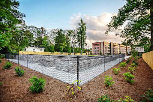 A fenced area with a building in the background and a house to the left.