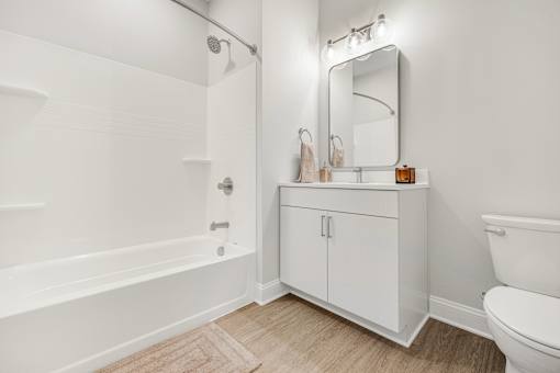 A white bathroom with a wooden floor and a white toilet. at Park Lamont Townhomes Apartments, Ohio