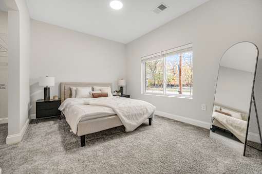 A bedroom with a large bed and a window overlooking a tree-lined street. at Park Lamont Townhomes Apartments, Ohio, 44106