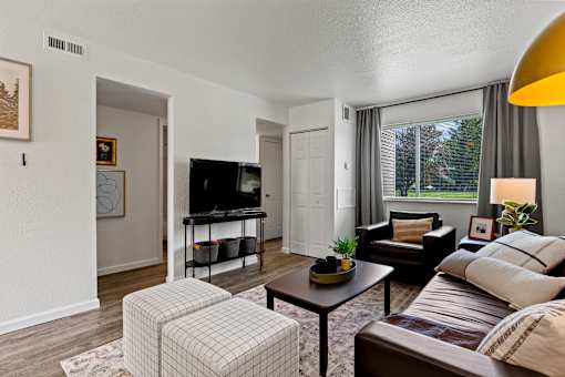 A living room with a brown couch, a white chair, and a television. at Vivo Toledo Apartments, Ohio, 43607