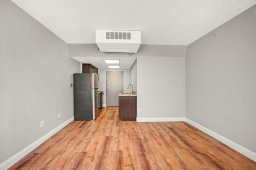 an empty living room with wood floors and a refrigerator