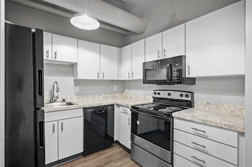 A black refrigerator is in a kitchen with white cabinets and a marble countertop.
