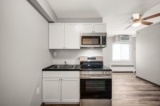 a kitchen with white cabinets and black appliances and a ceiling fan