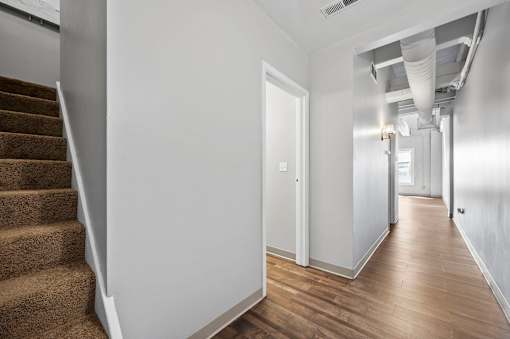 A hallway with a staircase on the left and a door on the right.