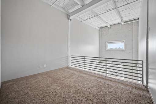 A room with a carpeted floor and a window with a metal railing.