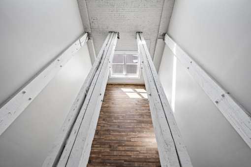 A long wooden staircase with metal handrails on both sides leading to a bright light at the top.