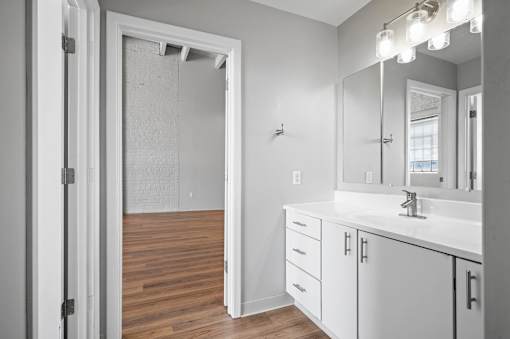 A bathroom with a white sink, mirror, and cabinets.