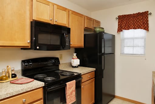 A black refrigerator sits in a kitchen with wooden cabinets.