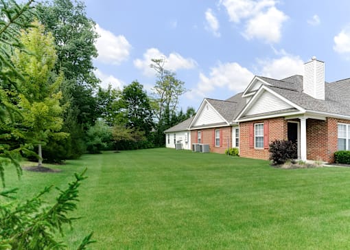 A house with a red brick exterior and a white roof is surrounded by a green lawn and trees.