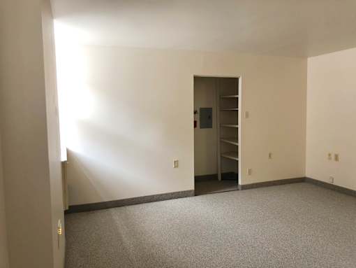 A room with a grey carpet and a white wall with a doorway leading to another room.