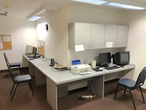 A room with a desk, chairs, and computers.