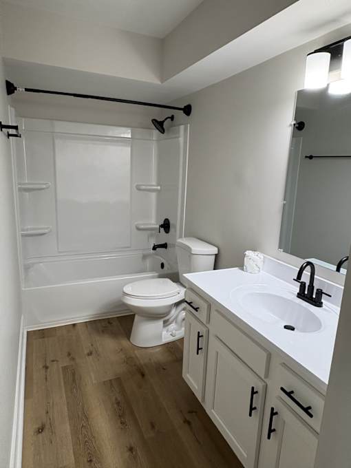 A white toilet is in a bathroom with wood floors.