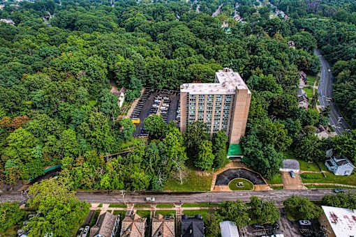 A large building surrounded by trees and a parking lot in front.