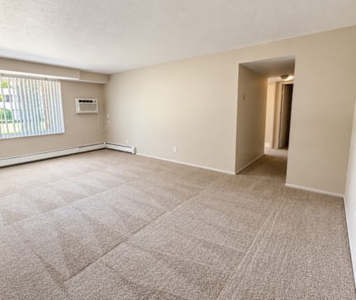 A spacious room with a carpeted floor and a window with blinds.