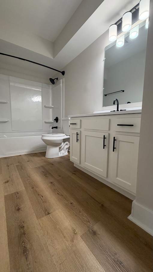 A white bathroom with a wooden floor and a white toilet.