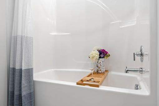 A white bathtub with a wooden tray holding a vase of flowers. at The Lumos Apartments, Cleveland, Ohio