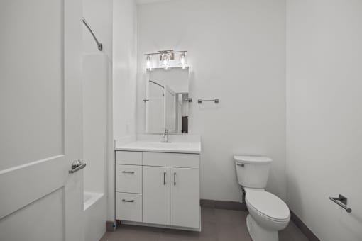 A white bathroom with a toilet, sink, and cabinet. at The Lumos Apartments, Cleveland