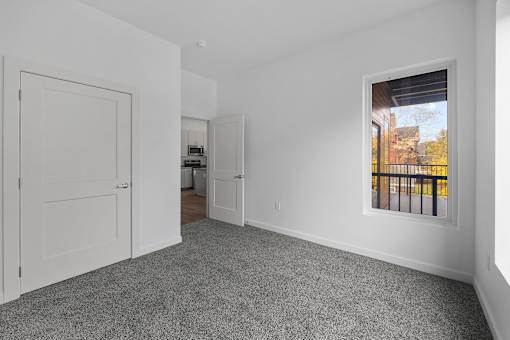 A room with a grey carpet and a window showing a balcony. at The Lumos Apartments, Ohio