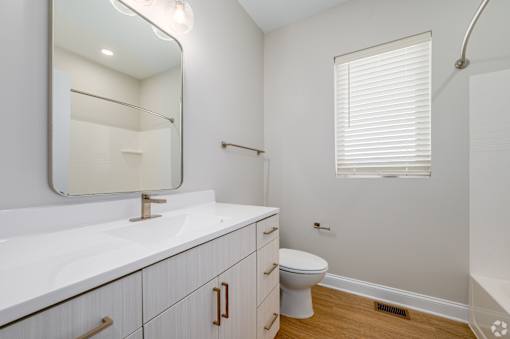 A white bathroom with a toilet, sink, and mirror. at Park Lamont Townhomes Apartments, Cleveland, OH, 44106