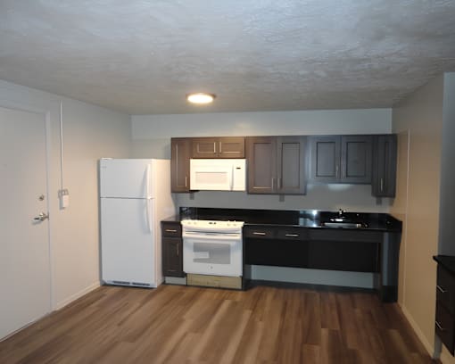 A kitchen with a white refrigerator, black countertops, and wooden floors.
