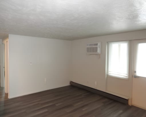 A room with a white ceiling, a window, and a wooden floor.