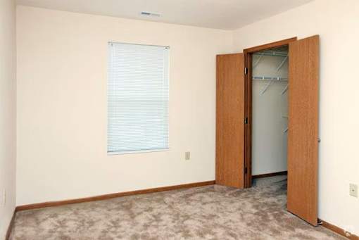 A room with a carpeted floor, a window with blinds, and a wooden door.