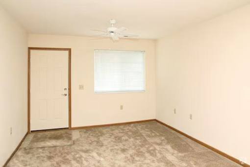 A room with a carpeted floor, a ceiling fan, and a window with blinds.
