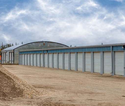 A long row of grey storage units with a dirt road in front.