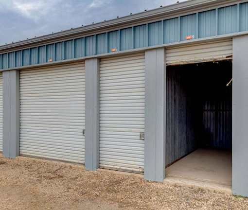 A storage unit with a closed grey door and an open door revealing a dark interior.
