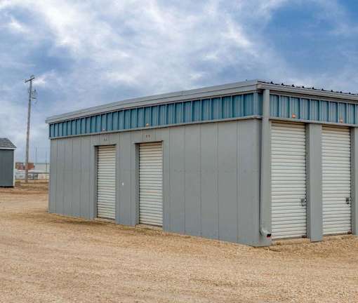 A grey storage building with three doors is situated in a field.
