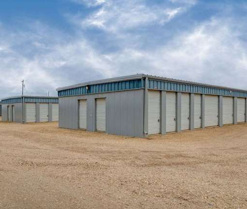 A series of grey storage units are lined up in a row on a dirt lot.
