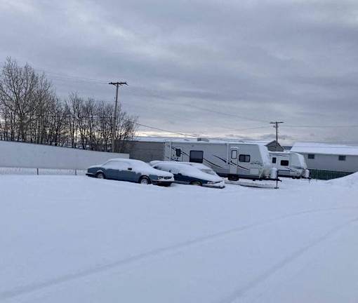A car is parked in the snow next to a trailer.