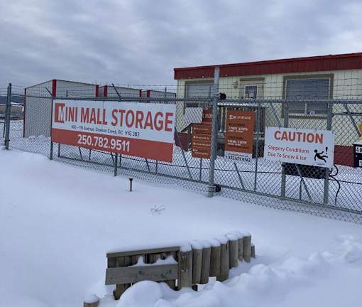A storage facility is covered in snow and has a caution sign for slippery conditions.